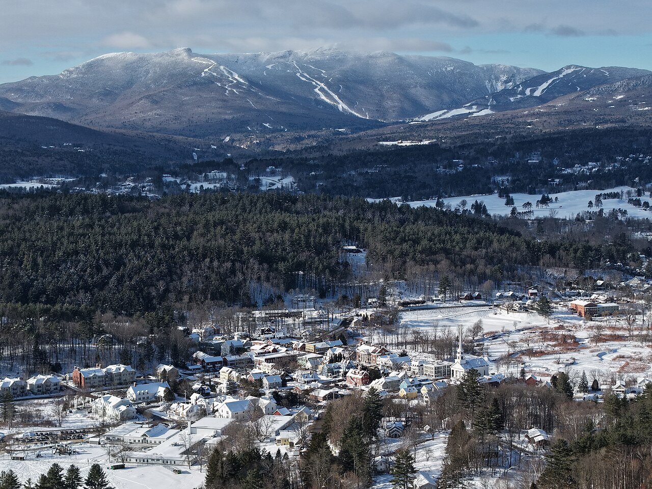 Stowe village from above under snow, with the Mansfield ridge and its trails behind.