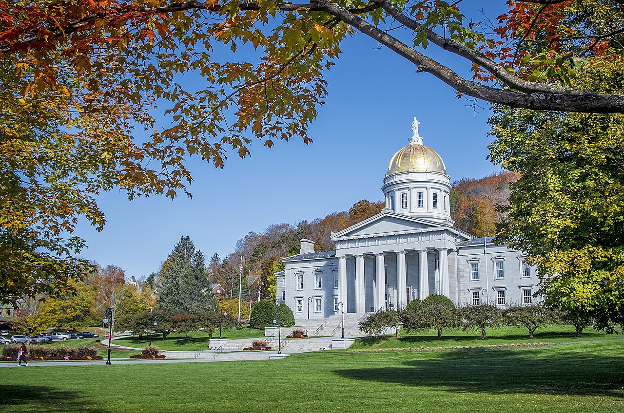 The State House in autumn, framed by a branch of red leaves.