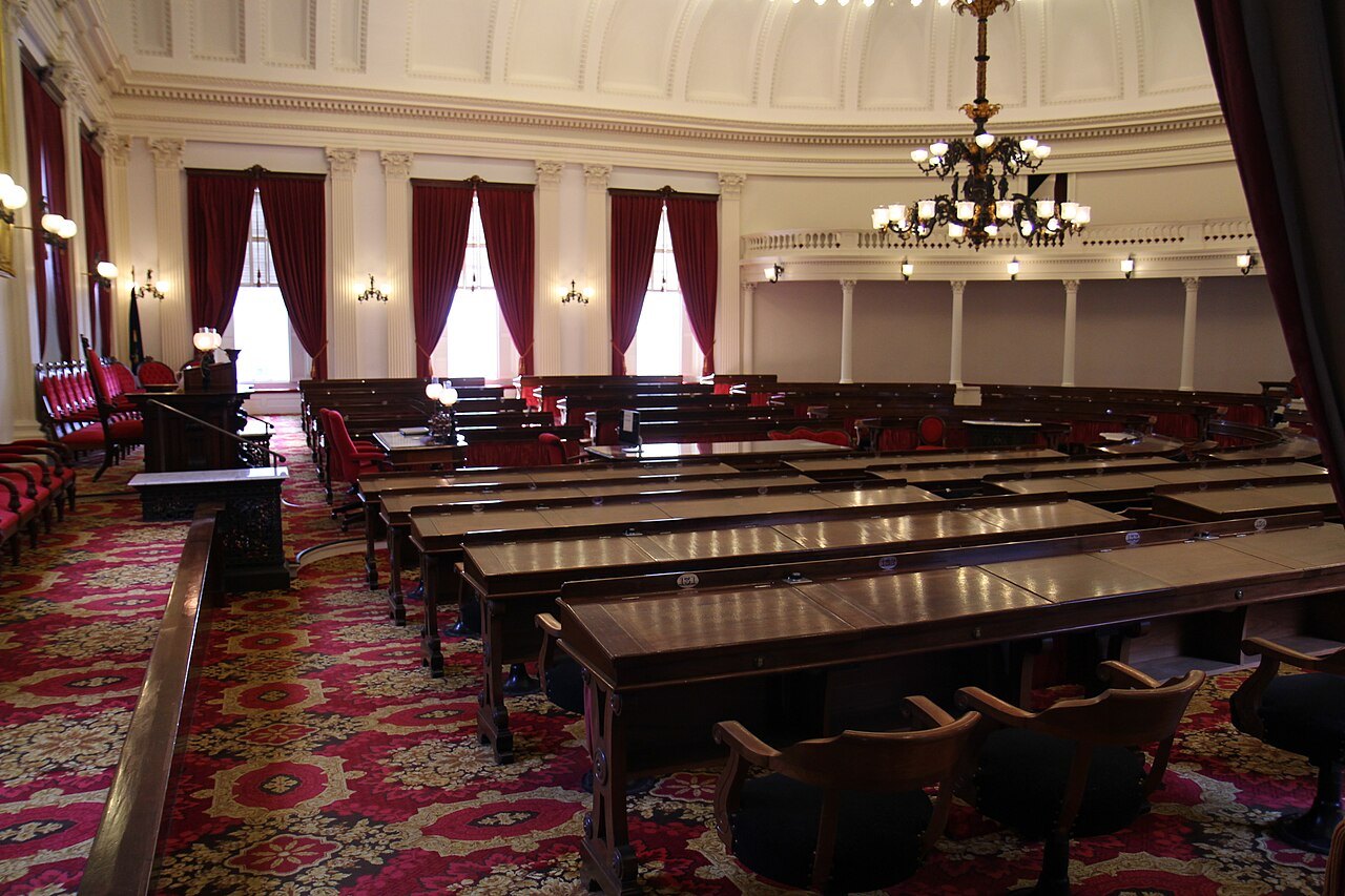 Representatives Hall under the dome, with rows of desks and a red patterned carpet.