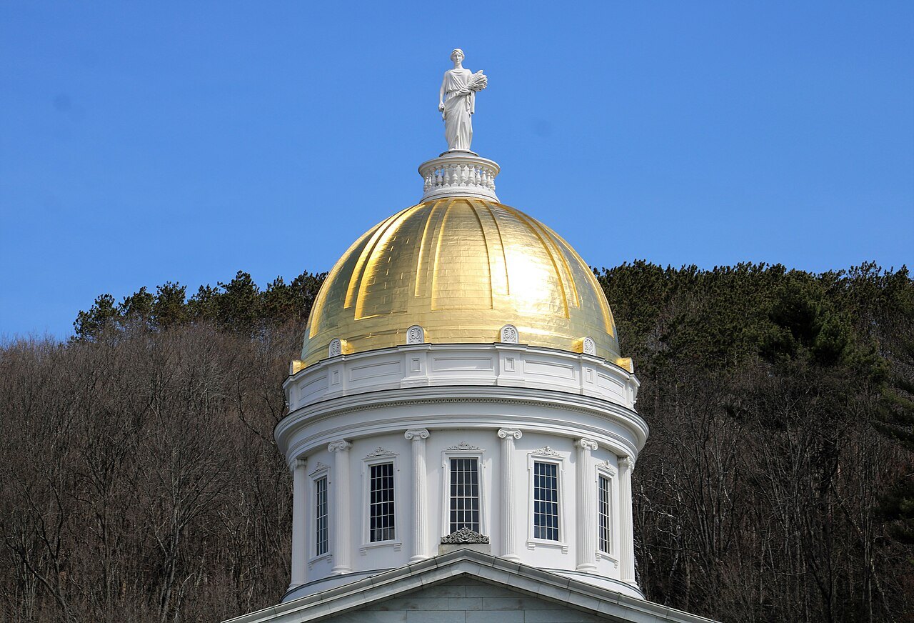 The gilded dome of the State House, topped by the statue of Ceres, against blue sky.