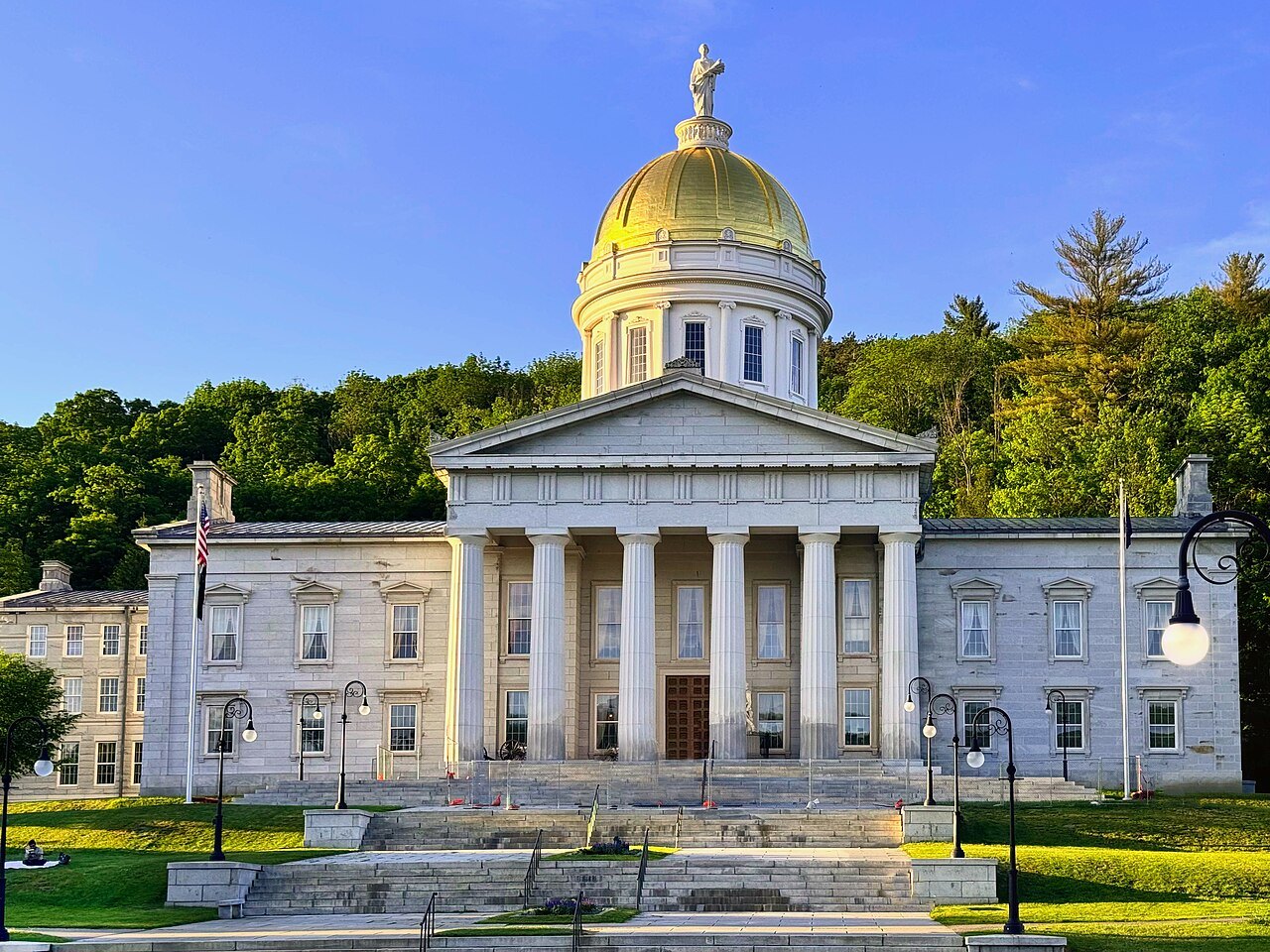 The State House at the head of its lawn, with lamp posts and purple flowers in front.