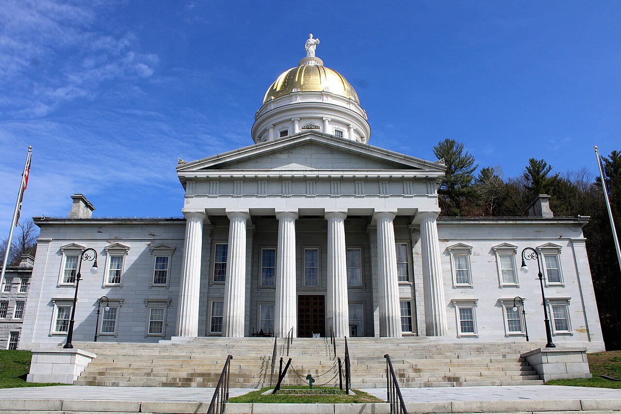 The State House facade, with the portico and the dome above, under a blue sky.