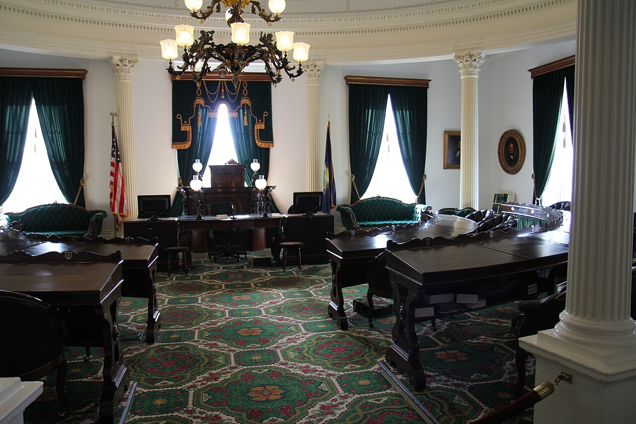 The Senate chamber of the State House, with its desks, chandelier and green drapes.