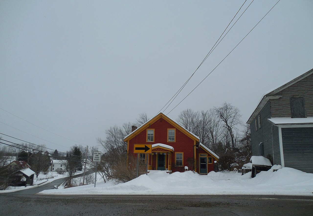 A red wooden building on a snow-banked road in Woodstock, with wires overhead.