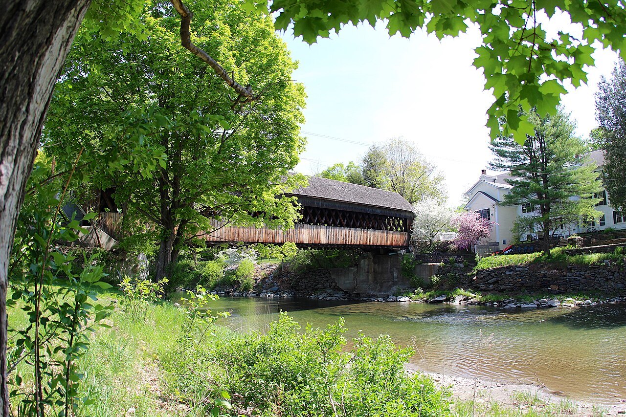 The Middle Bridge over the Ottauquechee River, a covered bridge seen across the water between spring trees.