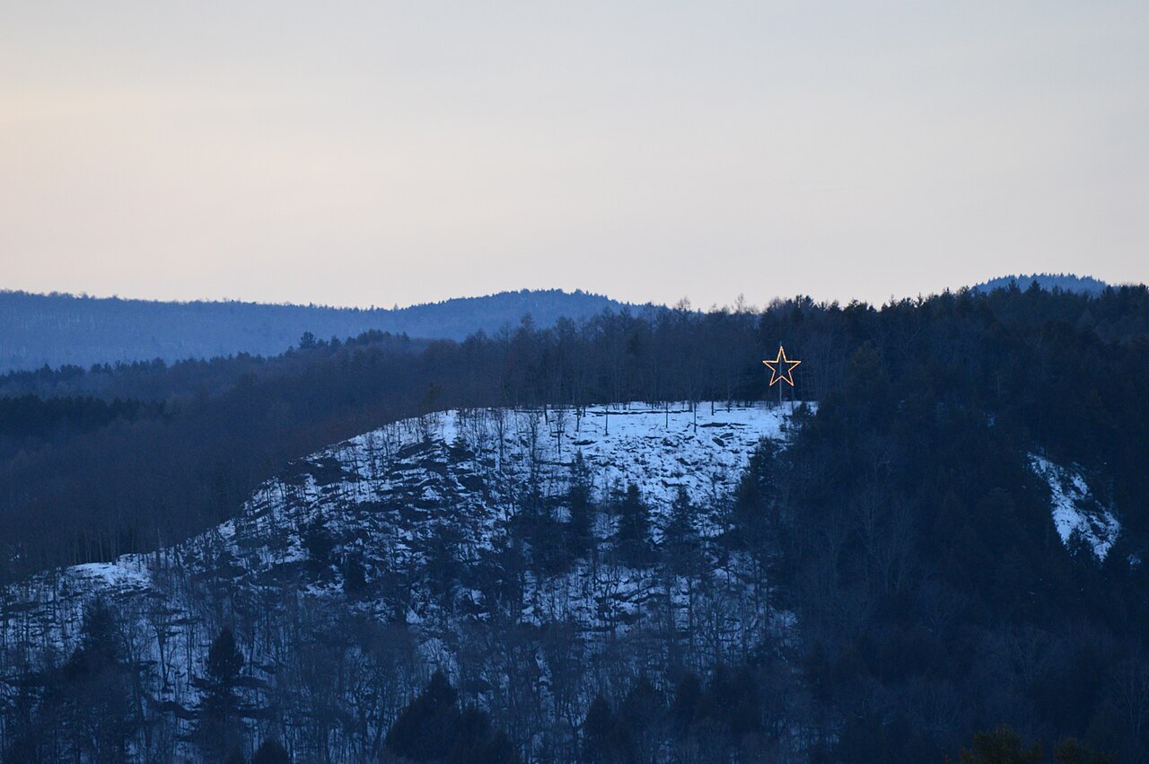 Mount Tom in winter, a snow-streaked cliff with a star on its ridge, above dark forest.