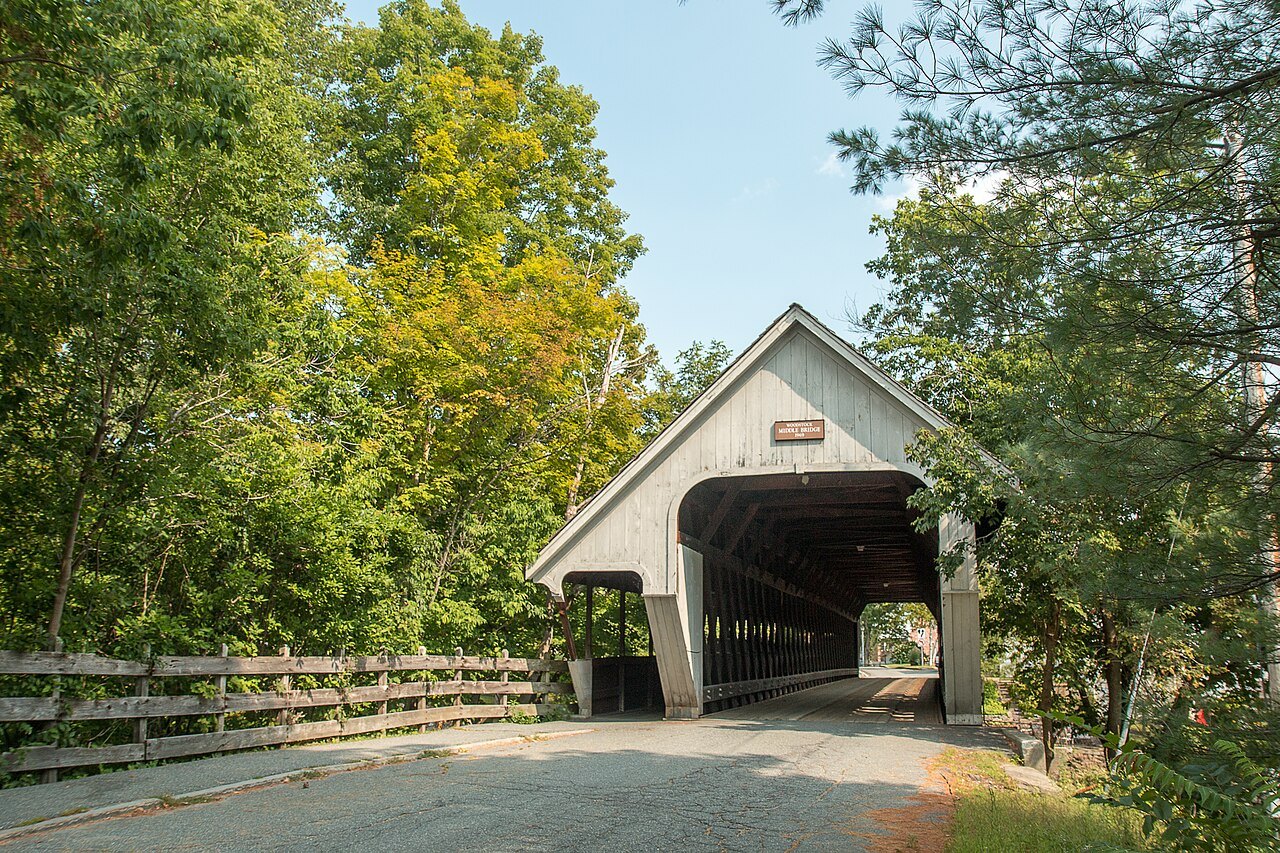 The Middle Bridge from the path, its covered span framed by green trees.